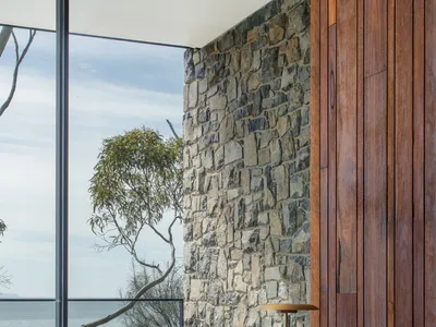 A modern home office with a stone wall, wooden desk, and leather chair.