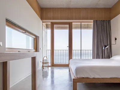 A modern bedroom featuring a clean, minimalist design with concrete flooring and wood accents.