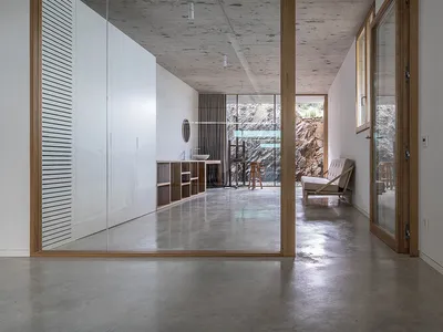 A minimalist bedroom with concrete walls and floor, featuring modern furniture and a large window.