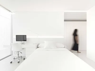 A minimalist bedroom with a white bed and desk.