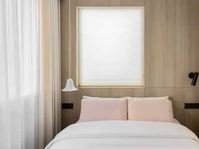 A minimalist bedroom with wooden walls, a white bed, and pink pillows.
