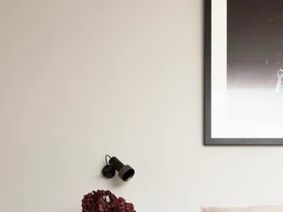 A minimalist bedroom with a white bed featuring textured cushions, situated on a wooden floor with a vase of red flowers on a
