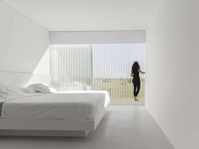 A modern bedroom with white walls and a glass window providing a view of the outdoors.