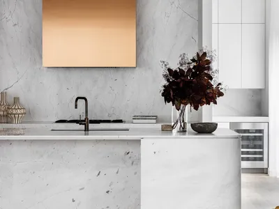 A modern kitchen with minimalist design, featuring marble countertops and a gold-hued backsplash.