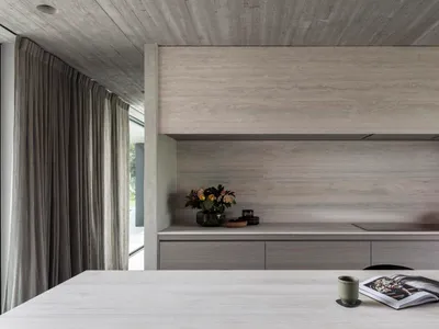 A modern, minimalist kitchen with concrete countertops and a large window.