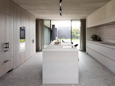 Modern, minimalist kitchen with concrete countertops and floor, featuring an island with a sink and a view of the outdoors th