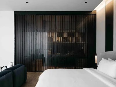 A modern minimalist bedroom featuring a metal wall, a bed with white sheets and gray headboard, and a large sofa with white p