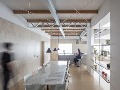 A modern minimalist dining kitchen with a white marble table and chairs, wooden flooring, and exposed wooden beams on the cei