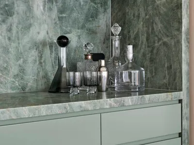 A modern bar counter featuring marble materials, with various glassware and decanters on a countertop.