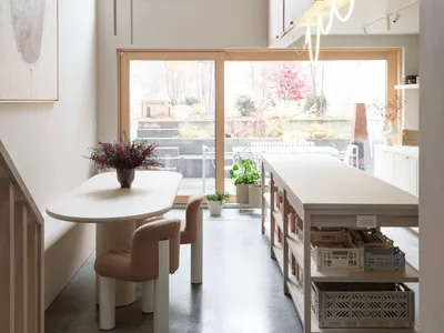 A minimalist residential kitchen with concrete flooring, a white dining table, and a large window.