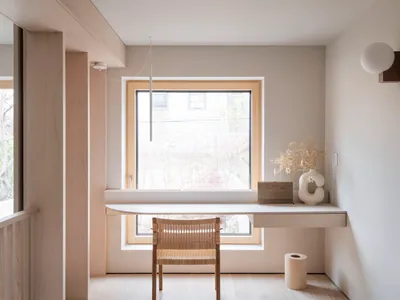 A minimalist home office with a small white desk, wooden chair, and a vase of flowers.
