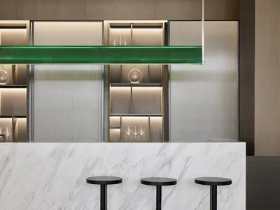 A modern bar counter featuring a green glass shelf, marble counter surface, and glass and metal accents.