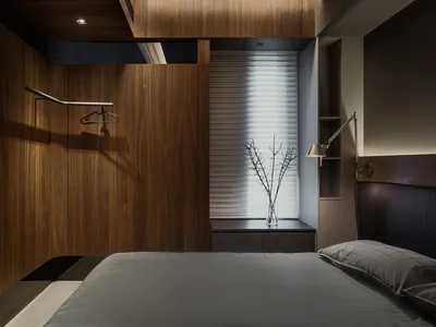 Modern minimalist bedroom featuring wooden-paneled walls and a neatly made bed with grey bedding.