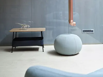 A modern living room featuring a metallic pipe and a small round pouf.