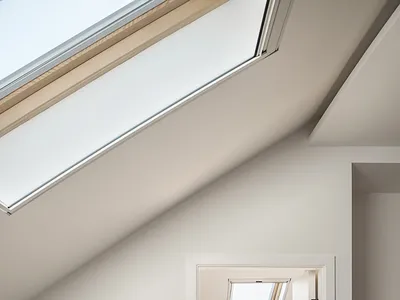 A minimalist bedroom featuring neutral-tones, white walls, and wooden elements with a skylight above, creating a serene and m