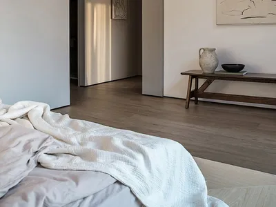 A minimalist bedroom featuring wooden furniture and a cotton blanket, with a modern light fixture and abstract artwork on the