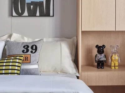 Bedroom with minimalist design featuring a bed with white sheets, colorful pillows, and a wooden headboard, with abstract art