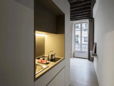 A sleek, modern kitchen with minimalist white cabinets, a sink, and a kettle on the stove.