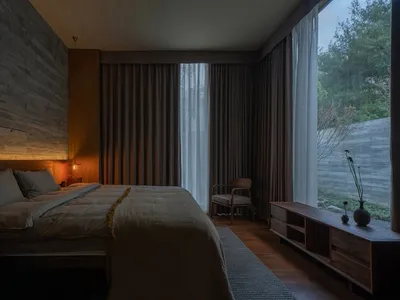 A minimalist bedroom featuring wooden elements and a large window with curtains.