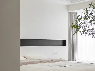 A minimalist bedroom with a wooden frame bed, white bedding, and a large potted plant by the window.