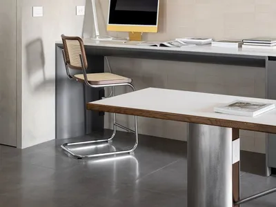 A minimalist home office featuring a concrete desk, a wooden chair, and a white pendant light.