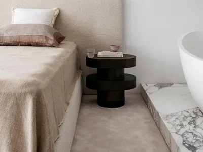 A minimalist bedroom featuring a fabric bed with a marble bedside table and brass wall fixtures.