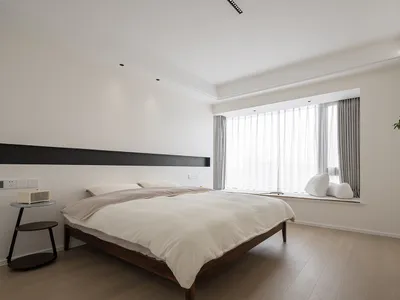 Modern minimalist bedroom with a queen-sized bed, white linens, and a large window with sheer curtains.