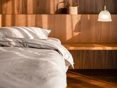 A bedroom with a wooden wall featuring a hanging lamp, a basket, and a neatly made bed with white bedding.