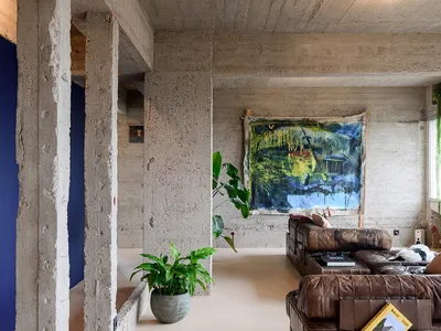 An industrial-style living room featuring exposed concrete walls and ceiling, a leather sofa, and a large abstract painting.