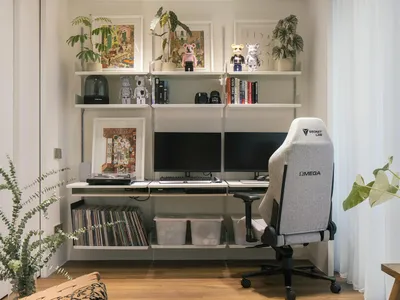 A modern and industrial home office featuring a grey gaming chair, multiple monitors, and decorative elements on shelves.