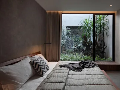 Modern bedroom with concrete walls, a large bed, and a garden view.