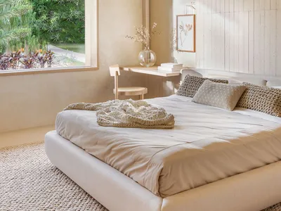 A minimalist bedroom featuring neutral colors with a large window overlooking greenery and a small workspace area.