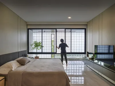A person standing in a modern minimalist bedroom with large glass windows, looking outside.
