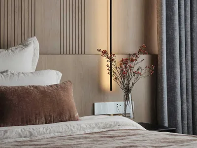 A modern bedroom with a bed, white and brown pillows, grey curtains, and a hanging light fixture.