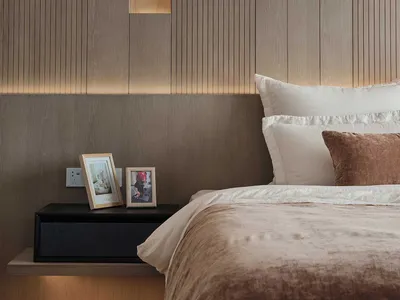A modern bedroom with wood paneling, featuring a neatly made bed with soft bedding and a floating nightstand with framed pict