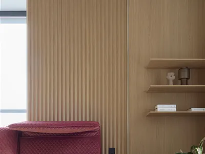 A minimalistic bedroom with a red velvet bed frame, wooden wall, and a circular bedside table with a plant.