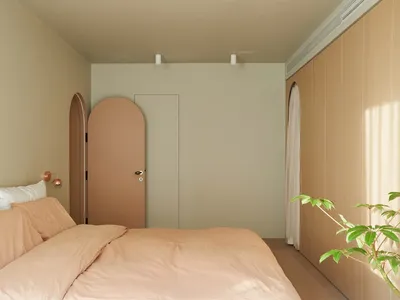 A minimalist bedroom with neutral-colored walls, a peach-colored bedspread, and a plant in a pot.