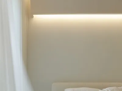A minimalist bedroom with neutral-toned upholstery, illuminated softly by a concealed light source.