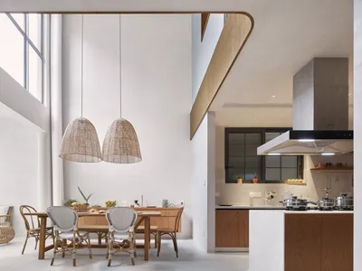 A modern, minimalist residential kitchen with concrete walls, wood cabinets, and rattan pendant lights.