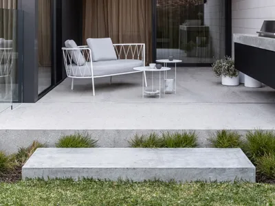 Modern industrial outdoor lounge area featuring a white metal chair with light grey cushions, a metal coffee table, and potte