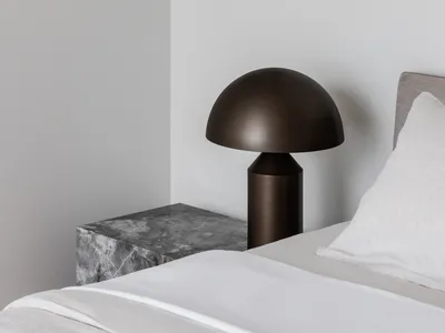 A minimalist bedroom featuring a modern metallic table lamp on a marble nightstand.