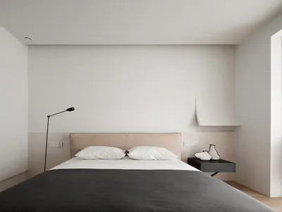 A minimalist bedroom with a large bed, two pillows, a lamp, and a nightstand.
