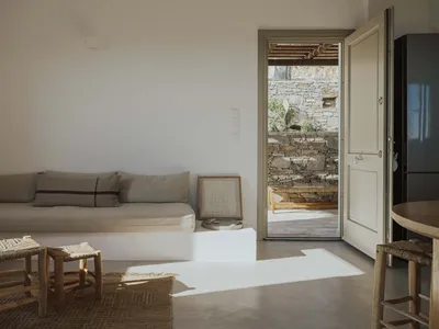A modern, minimalist living room with concrete flooring, wooden furniture, and stone accents