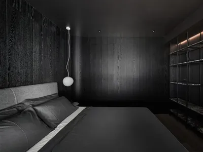 A minimalist black bedroom with wooden walls and a grey bed.