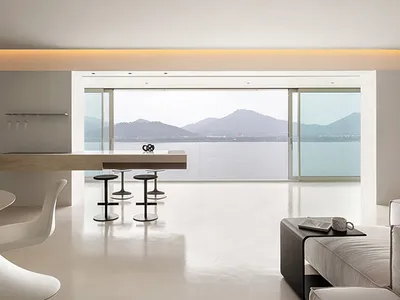 Modern minimalist living room with concrete flooring, minimalist furniture, and large windows overlooking mountains.