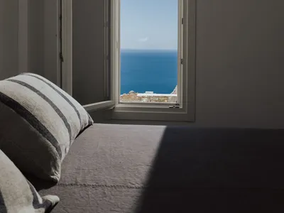 Minimalist bedroom with cotton fabric bedding, overlooking the ocean through an open window.