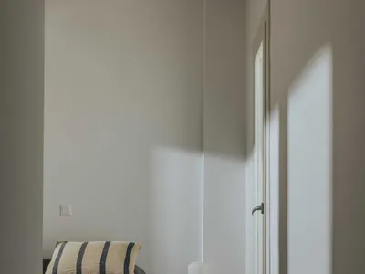 A minimalist bedroom with a concrete floor, a single nightstand with a lamp, and a striped pillow.