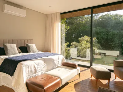 Bedroom featuring minimalist decor with leather furniture and fabric bedding, large glass windows overlooking greenery.