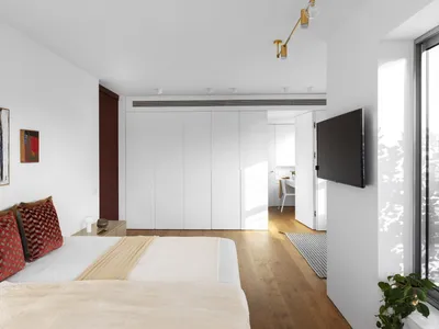 A modern, minimalist bedroom with a white bed, wooden floor, and minimalist decor.