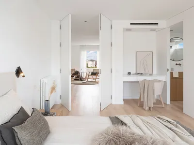 A minimalist bedroom with wooden floors and a bed dressed in neutral tones, featuring a study area and an open layout.